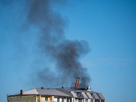 Huge black smoke from burning residential building roof against blue sky.の写真素材