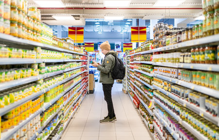 Male customer perusing food items on supermarket shelves in grocery store. Man looks at price and choose organic food.の写真素材