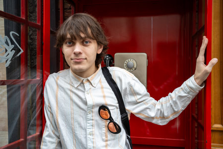 Young man in front of red telephone booth, London.の写真素材