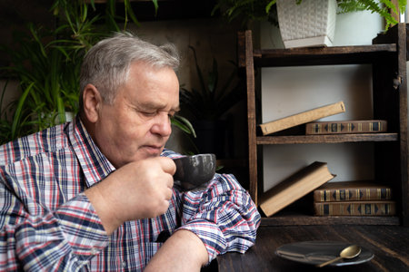 Elderly man deeply enjoying his coffee in rustic cafe setting with greenery and bookshelf.の写真素材