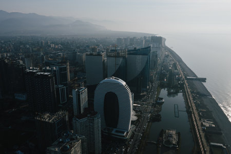 Aerial view of modern Batumi city skyline against a mountain backdrop, illuminated by the morning sun, reflecting off the buildings and ocean.の写真素材