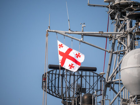 Georgian flag fluttering on naval ship radar tower, with intricate communication equipment against blue skyの写真素材