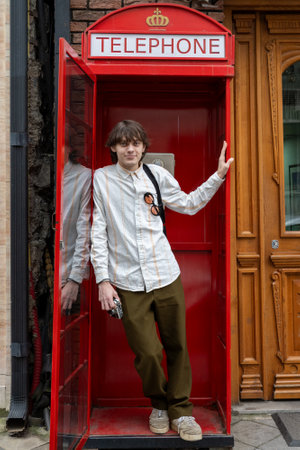 Smiling young man with vintage camera posing in iconic red telephone box.の写真素材