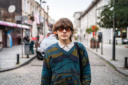 Young man in 90s fashion with oversized sunglasses stands confidently in bustling urban environment.の写真素材