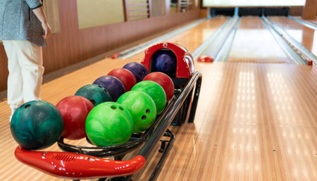 Bowling player contemplating over assorted colorful bowling balls on alley rack.