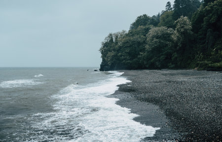 Misty beach view with gentle waves washing over pebbled shore under cloudy skies creates serene and tranquil seascape.の写真素材