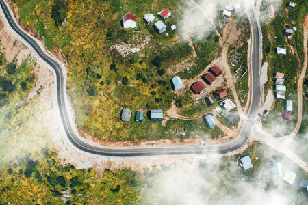 Top-down drone shot of curved mountain road through small, mist-enshrouded village of Gomismta.の写真素材