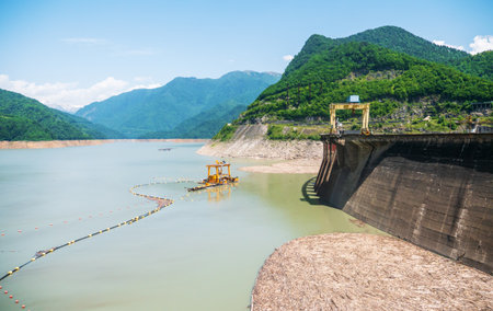 Enguri dam with operational crane and floating barrier system, set against a backdrop of lush...