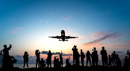 Silhouette of people watching taking pictures of airplane flying overhead at sunset.の写真素材
