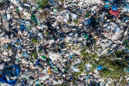 Aerial top view of large urban landfill filled with various types of waste and scattered greenery,...