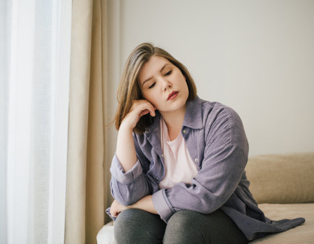 Thoughtful plus-size woman resting head on hand, in deep contemplation. Calm indoor setting, self-reflection, and peaceful atmosphere. Casual home attire.の写真素材