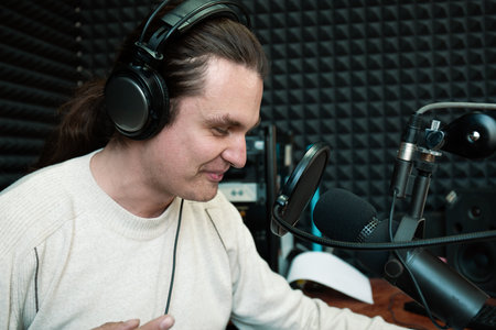 Podcaster in soundproof studio recording podcast episode in headphones and speaking into professional microphone, ideal for media production, audio projects, and podcasting content creation.の写真素材