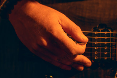 Hand strumming electric guitar strings in warm ambient light, musician focus and instrument details.