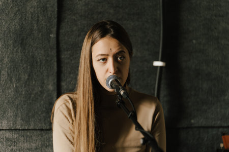Young woman singing into microphone in recording studio, conveying focus and passion in her performance.の写真素材
