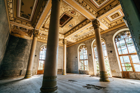 Empty, decaying ballroom featuring tall columns, arched windows, and intricate ceiling designs in historic, abandoned building.の写真素材
