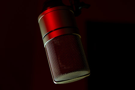 Studio microphone with red lighting against a dark background. Close-up shot of professional condenser microphone for recording and podcasting. Music and audio production concept.の写真素材