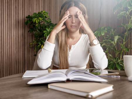 Woman feeling stressed while studying at desk with books and tablet. Indoor scene. Learning, education, and stress concept.の写真素材