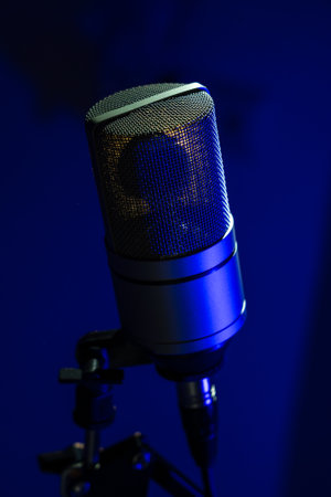Studio condenser microphone close-up against a dark blue background, emphasizing texture and professional audio equipment details.の写真素材