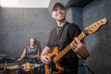 Man playing guitar with smiling expression, accompanied by drummer in soundproof rehearsal room.の写真素材