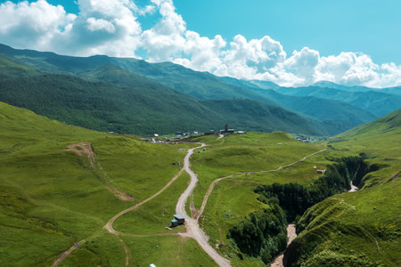 Majestic mountainous region in Mestia, Georgia with rolling hills, winding path, and traditional tower under bright sky, evoking sense of discovery and peace.の写真素材