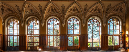 Gothic-style abandoned building interior with tall ornate arched windows, intricate ceiling details, and decayed wooden panels. Sunlight streams through broken windows, highlighting the forgottenの写真素材