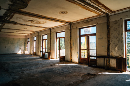 Abandoned Soviet resort interior with large windows, peeling ceilings, and scattered debris, showcasing silent echoes of past grandeur in sunlit vacant space.の写真素材