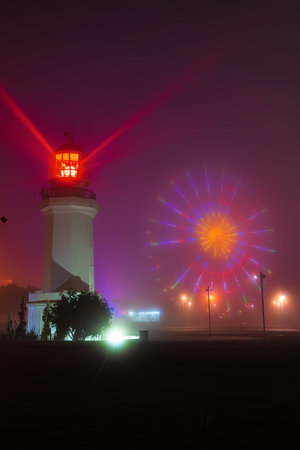Lighthouse and Ferris wheel glowing through dense fog in magical night scene in Batumi, Georgia.の写真素材