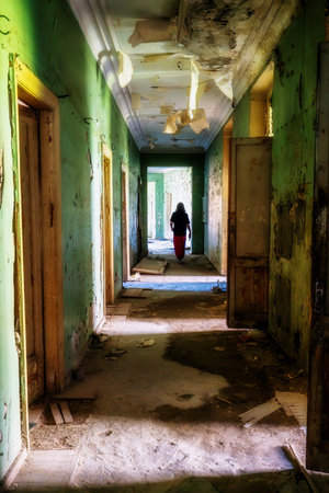 Abandoned building hallway with woman silhouette, urban exploration, mental health, loneliness, decay, post-apocalyptic concept, eerie light, horror atmosphere, peeling paint.の写真素材
