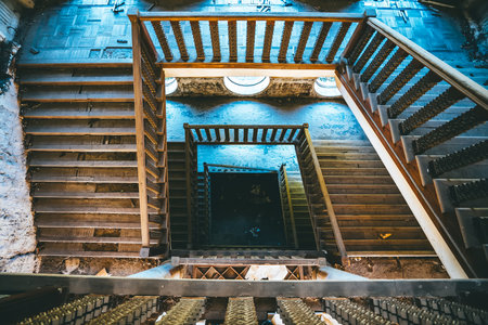 Top view of spiral staircase in abandoned building with ornate railing and circular windows,...