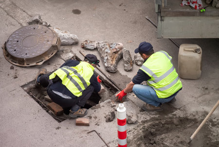 Utility workers repairing underground manhole, performing urban road maintenance, infrastructure...