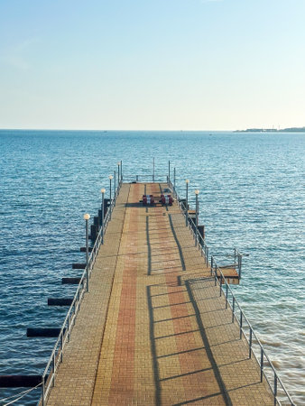 Vertical aerial view of empty pier extending over calm sea, evoking peaceful travel, minimalism, solitude and architectural geometryの写真素材