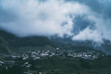 Mountain village under dramatic cloudy sky, rural life landscape, travel destination, scenic foggy hills.の写真素材