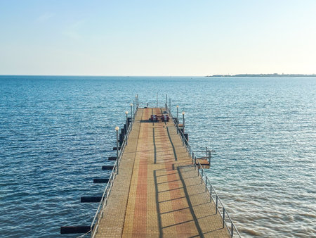 Symmetrical view of long pier stretching into sea under clear sky, perfect for themes of travel, solitude, symmetry, and calm seascapesの写真素材