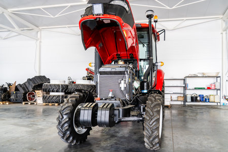 New tractor with open hood inside bright modern workshop for engine diagnostics, machinery maintenance, agricultural equipment inspection.の写真素材