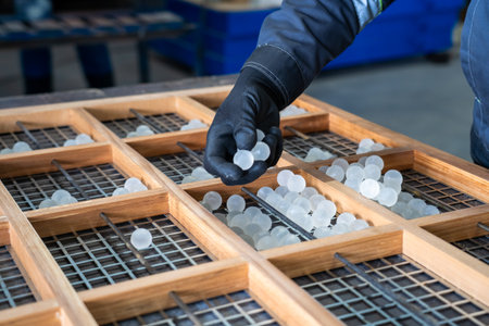 Industrial worker sorting translucent polymer balls on grid for manufacturing, recycling and...