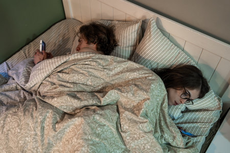 Couple lying in bed ignoring each other while using smartphones, illustrating digital addiction, relationship problems, emotional disconnection and modern lifestyle issues.の写真素材