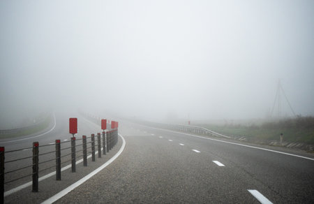Foggy road disappearing into mist. Danger, uncertainty travel, climate risks and road safety in low visibility conditions.の写真素材