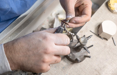Dental technician processing metal-ceramic crowns on dental model using rotary tool in laboratory,...