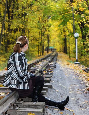 Young women sits on a rails n a autumn forestの写真素材