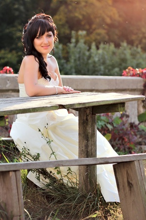 Girl in the wedding dress sitting on the bench neat the tableの写真素材