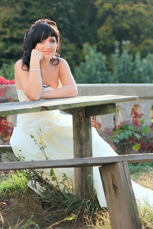 Girl in the wedding dress sitting on the bench neat the tableの写真素材