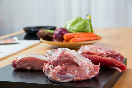 Meat parts on the table with vegetables at backgroundの写真素材