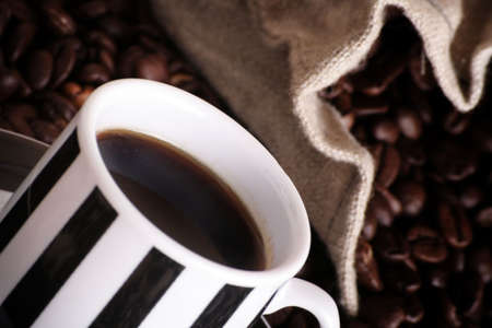 some coffee beans and a jute sack behind a cup of black coffee