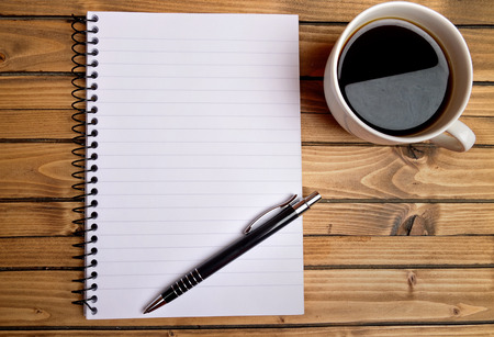 Notepad with coffee on wooden tableの写真素材