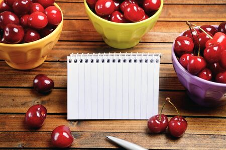 Notebook and colorful bowl with cherries on tableの写真素材