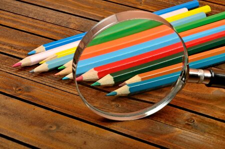 Magnifying glass with colorful pencil on wooden tableの写真素材