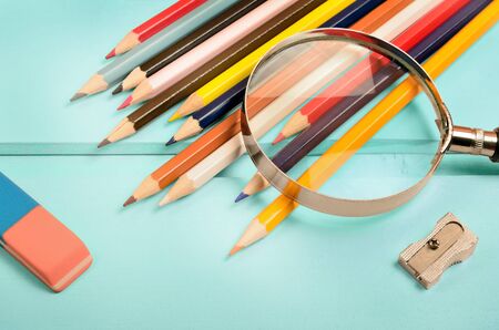 Magnifying glass with colorful pencil on blue wooden tableの写真素材