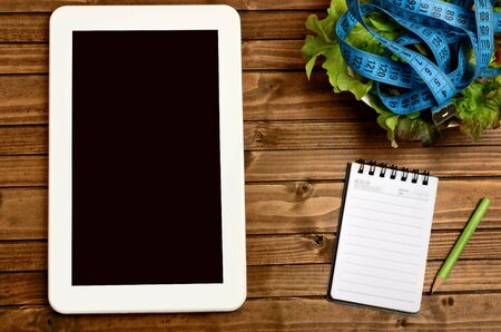 Vegetable salad with tablet and notepad on wooden tableの写真素材