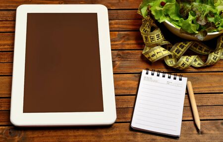 Notebook tablet and vegetable salad on wooden table