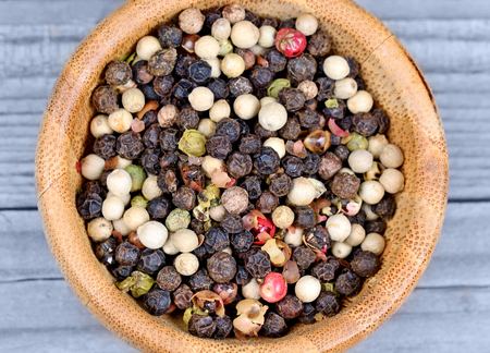 Colorful peppercorns in a bamboo bowl on blue wooden table